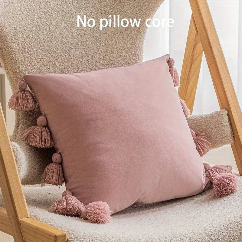 Coussin déco en velours rose avec pompons, posé sur une chaise en bois dans un salon moderne