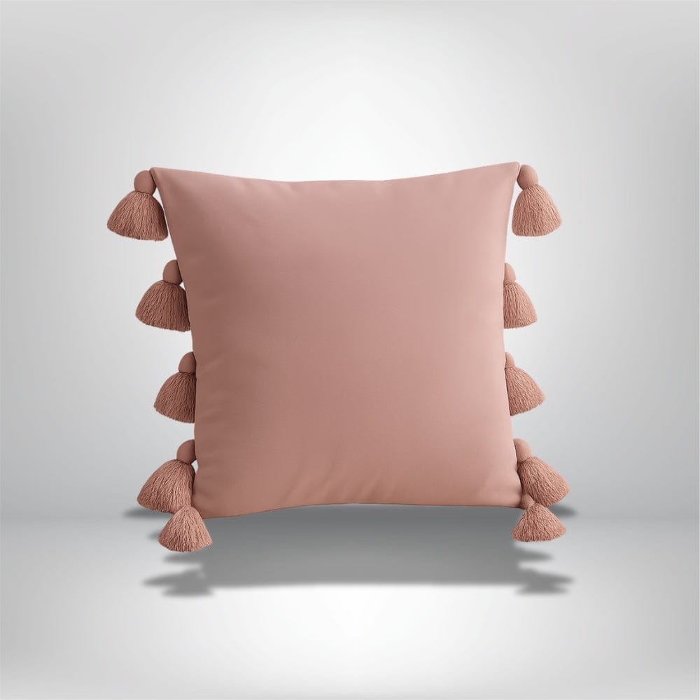 Coussin décoratif rose en velours avec pompons, posé sur un fond neutre, idéal pour un canapé ou une chambre