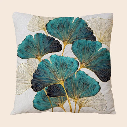 Coussin décoratif aux motifs de feuilles turquoise et dorées sur fond clair, posé sur un canapé moderne