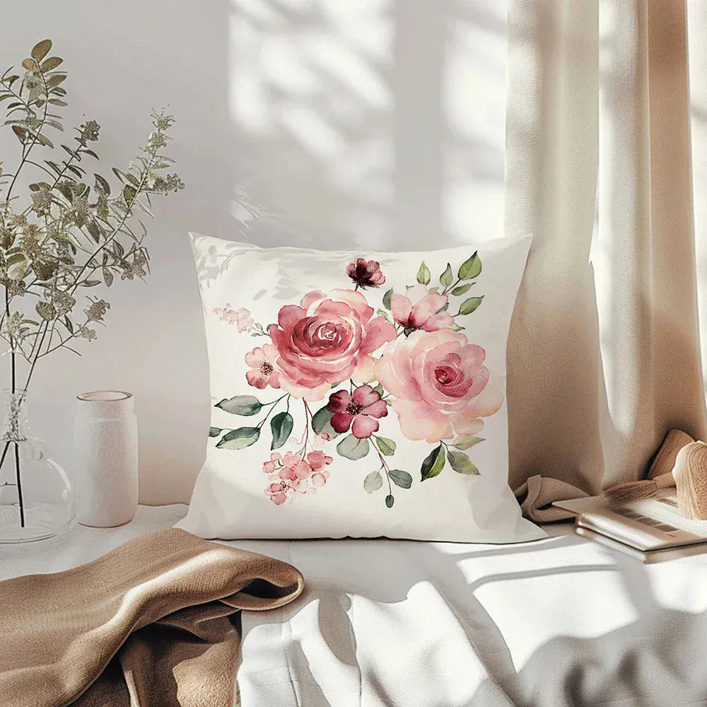 Coussin décoratif à motifs floraux roses sur fond crème, posé sur un canapé avec une couverture beige