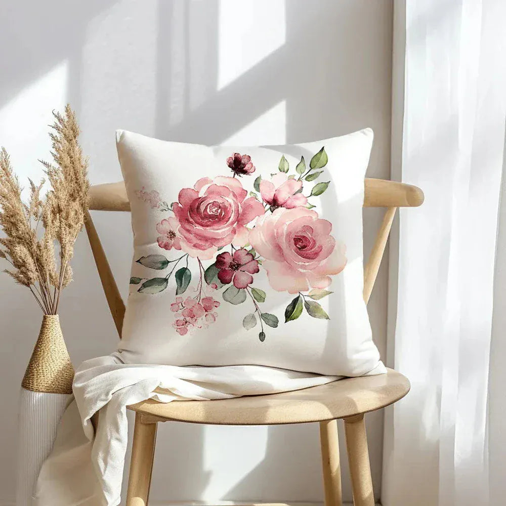 Housse de coussin décorative avec des fleurs roses sur fond crème, posée sur une chaise en bois