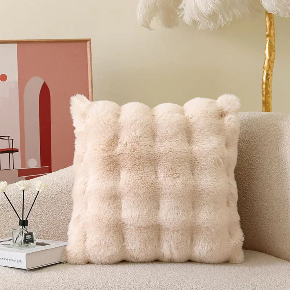 Coussin décoratif en fourrure beige, avec un motif matelassé, posé sur un canapé doux et moderne