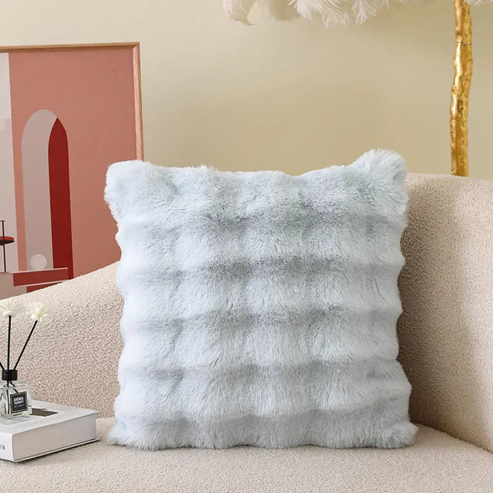 Coussin décoratif en fourrure bleue, posé sur un canapé beige, avec un motif texturé et doux au toucher