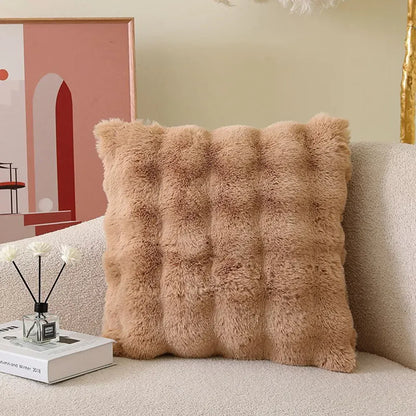 Coussin déco en fourrure beige, avec un motif texturé, posé sur un canapé clair dans un salon moderne