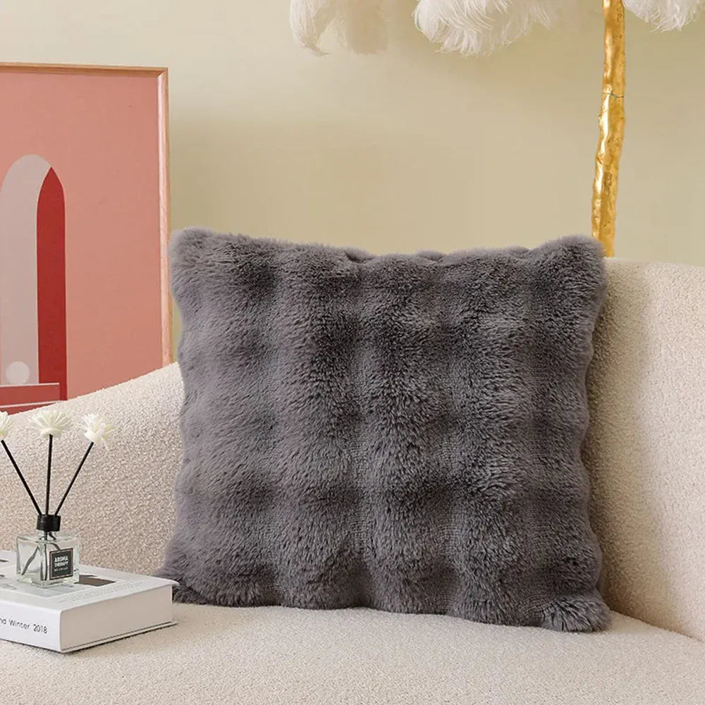 Coussin déco en fourrure gris, avec un motif texturé, posé sur un canapé beige dans un salon moderne