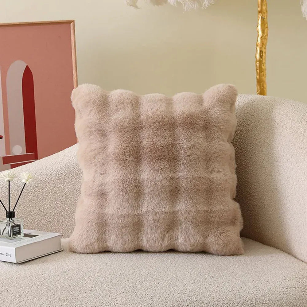 Coussin décoratif en fourrure beige, à motifs carrés, posé sur un canapé moderne et texturé