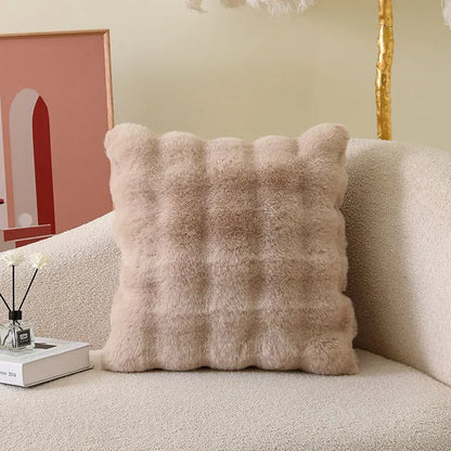 Coussin décoratif en fourrure beige, à motifs carrés, posé sur un canapé moderne et texturé