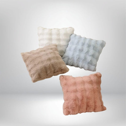 Quatre coussins décoratifs en fourrure aux couleurs pastel, disposés sur un fond neutre, parfaits pour un canapé ou un lit