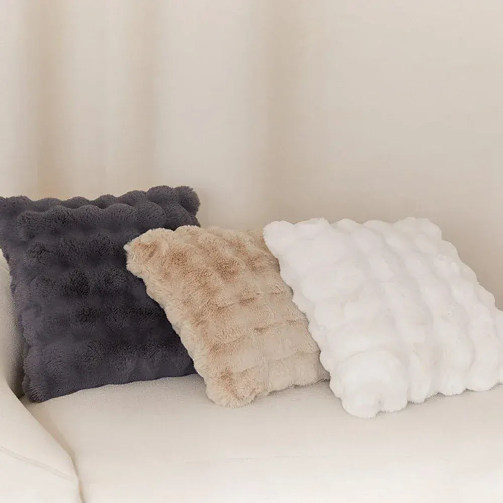 Trois coussins décoratifs en fourrure, gris, beige et blanc, posés sur un canapé clair