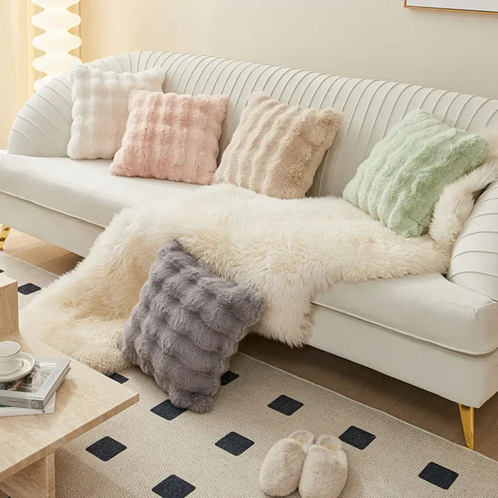 Coussins décoratifs en fourrure aux teintes pastel sur un canapé blanc, avec un plaid doux en dessous