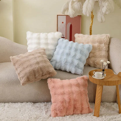 Coussins décoratifs en fourrure aux teintes pastel, disposés sur un canapé dans un salon chaleureux