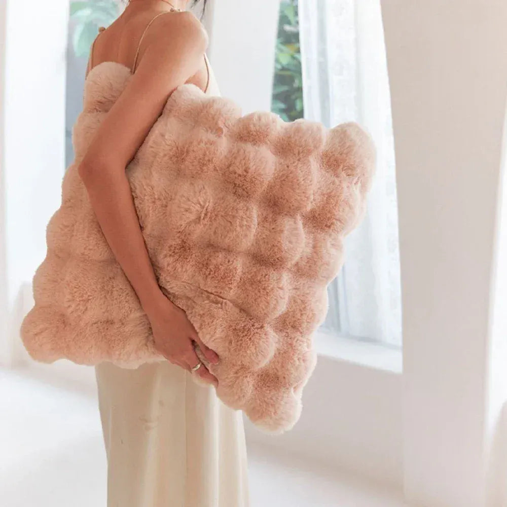 Coussin décoratif en fourrure rose, forme originale et douce, porté devant une fenêtre lumineuse