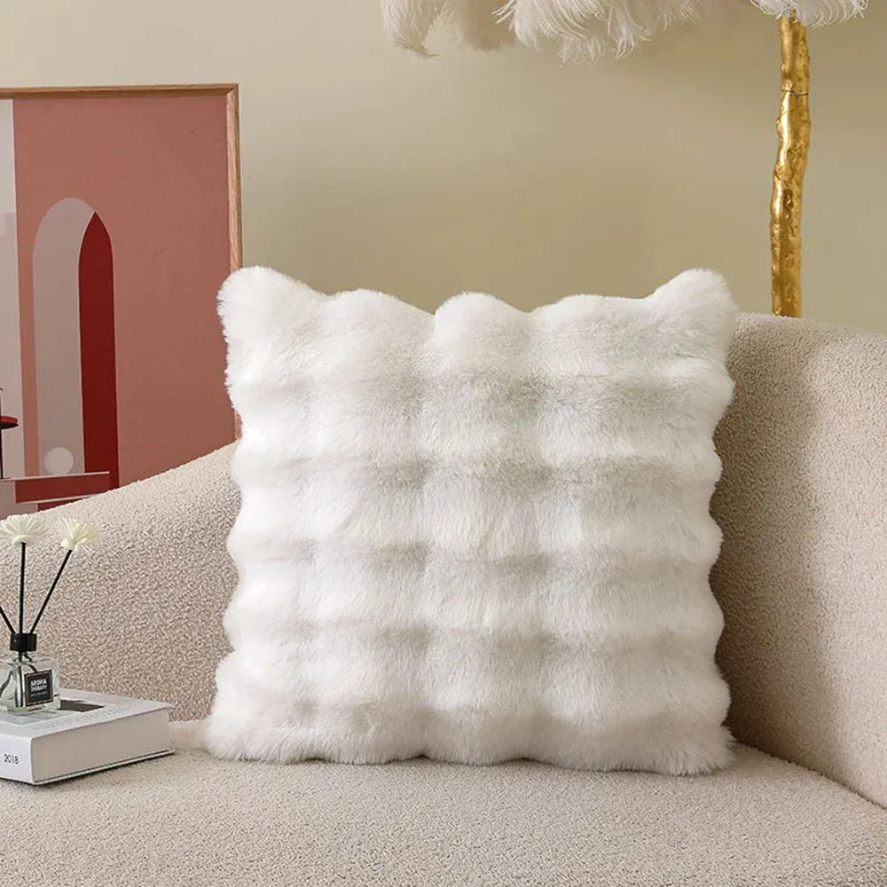 Coussin décoratif en fourrure blanche, aux formes ondulées, posé sur un canapé beige dans un salon moderne