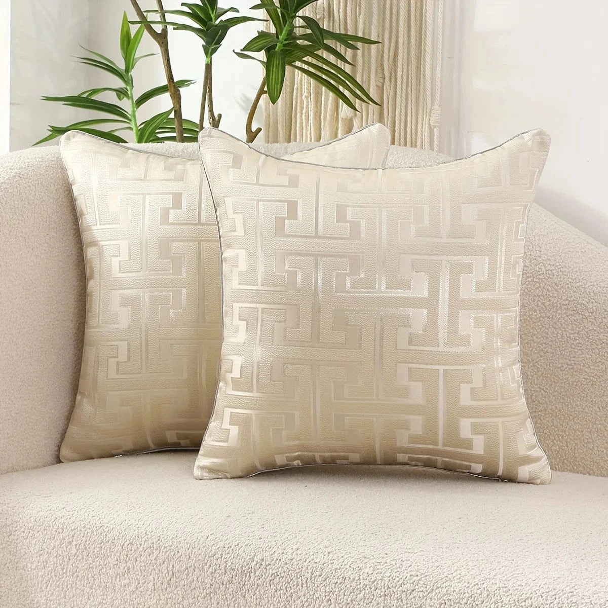Deux coussins décoratifs en tissu beige avec un motif géométrique moderne, posés sur un canapé doux