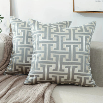 Coussins décoratifs en tissu argenté avec motifs géométriques, posés sur un canapé moderne et élégant