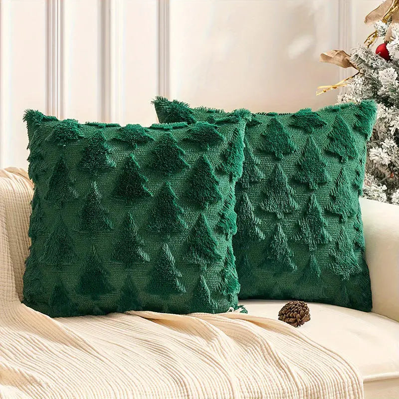 Deux coussins décoratifs verts en velours avec motifs de sapins, posés sur un canapé beige
