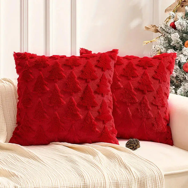 Deux coussins décoratifs rouges en velours avec motifs de sapins, posés sur un canapé beige