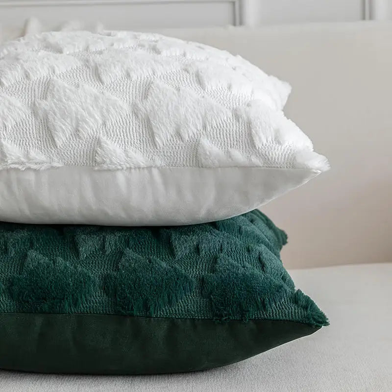 Coussins décoratifs en velours vert et blanc, motifs sapins, posés sur un canapé clair