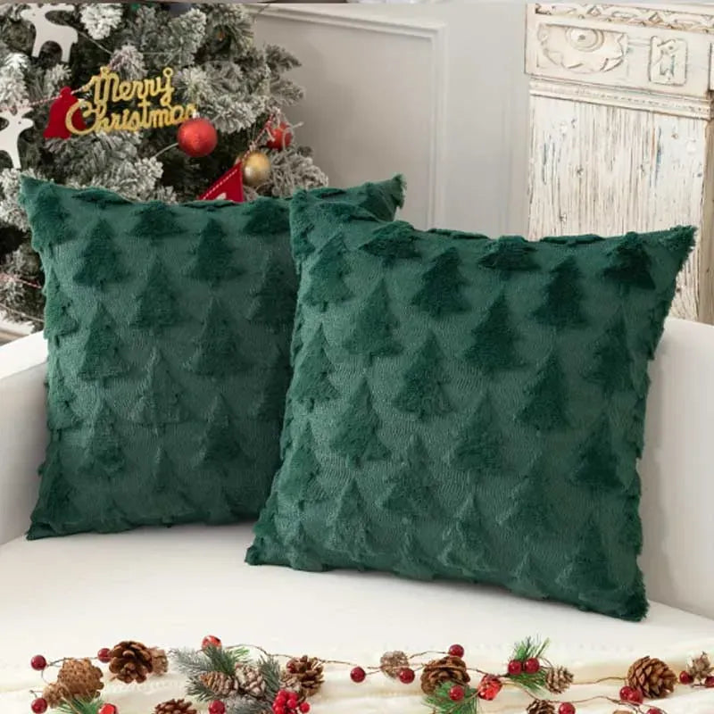 Deux coussins décoratifs en velours vert, ornés de motifs de sapins, posés sur un canapé blanc