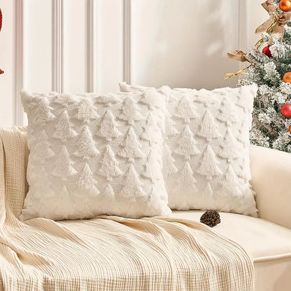 Deux coussins décoratifs blancs avec motifs de sapins, posés sur un canapé, entourés d'une ambiance festive