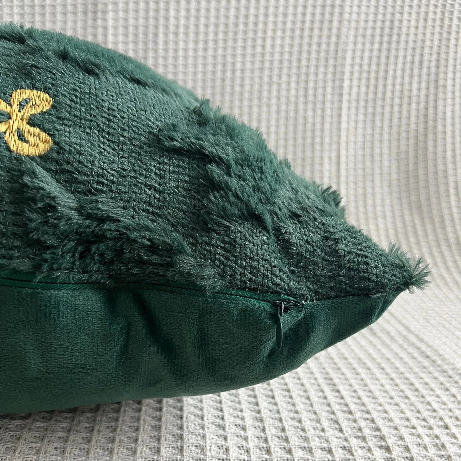 Coussin déco vert en matière douce avec broderies dorées, posé sur un fond texturé clair