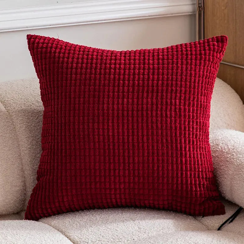 Coussin décoratif rouge en velours texturé posé sur un canapé beige, ajoutant une touche chaleureuse à l'intérieur