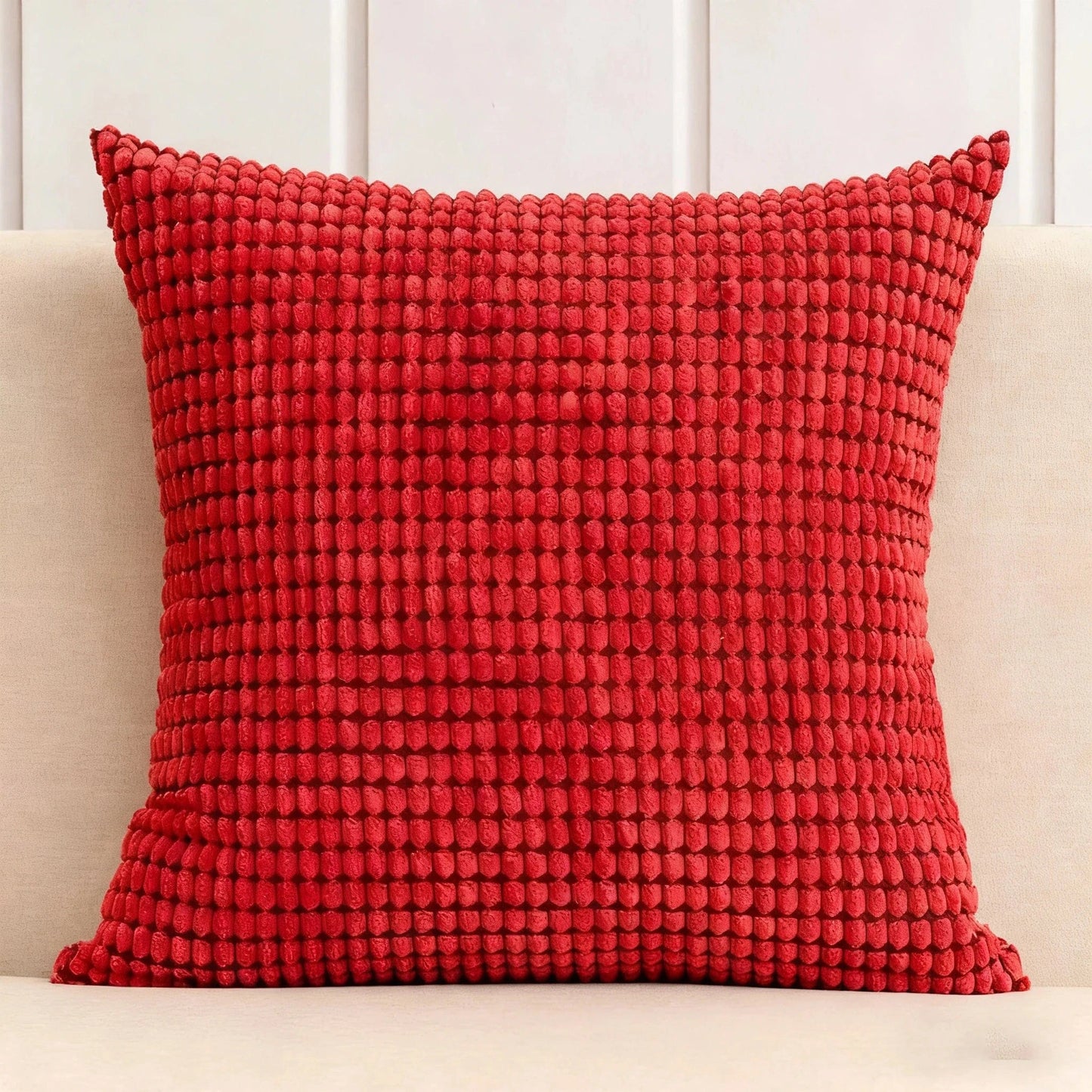 Coussin décoratif rouge texturé posé sur un canapé beige, ajoutant une touche chaleureuse à l'espace