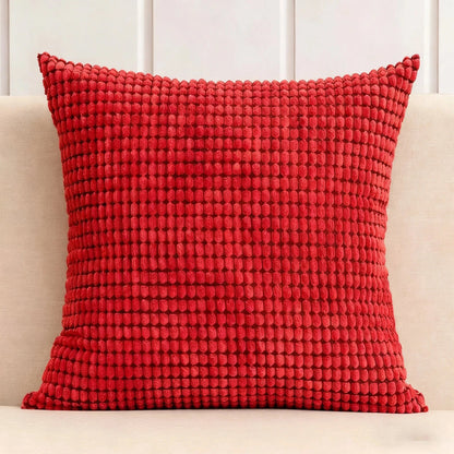 Coussin décoratif rouge texturé posé sur un canapé beige, ajoutant une touche chaleureuse à l'espace