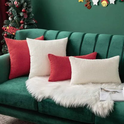 Coussins décoratifs rouges et blancs en tissu texturé, disposés sur un canapé vert avec un plaid en fausse fourrure