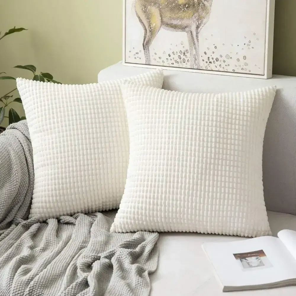 Deux coussins décoratifs blancs à texture en relief, posés sur un canapé avec un plaid gris