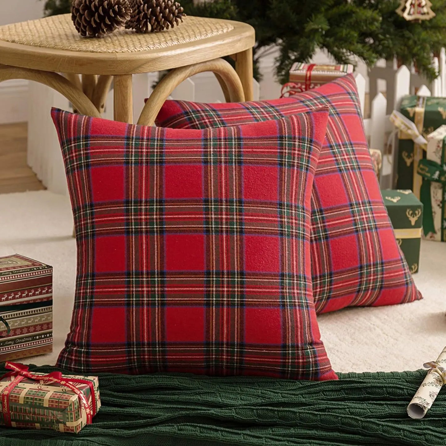 Coussins décoratifs en tartan rouge et vert, posés sur un tapis vert, entourés de cadeaux de Noël