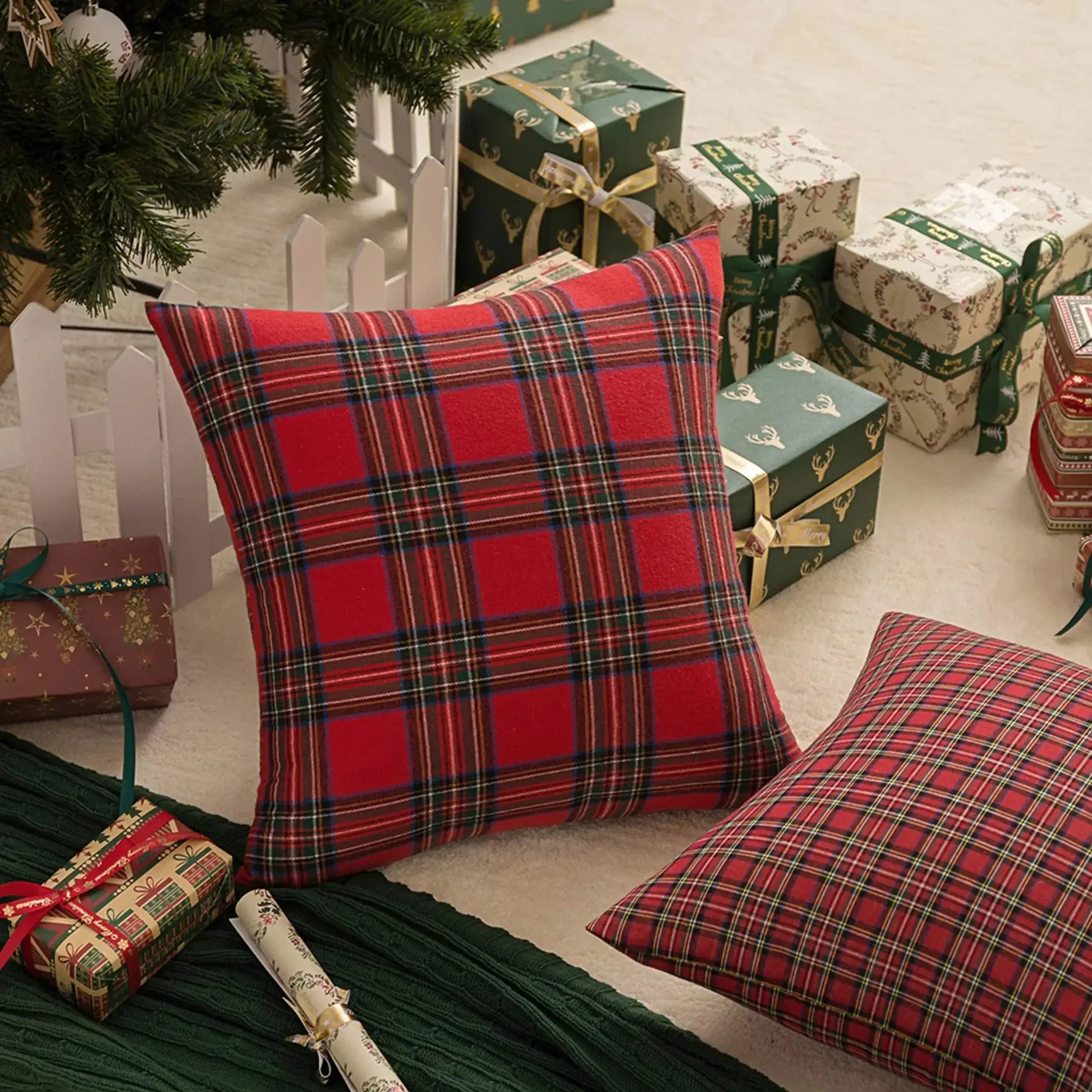 Coussins décoratifs à motifs tartan rouge, posés sur un tapis, entourés de cadeaux sous un sapin de Noël