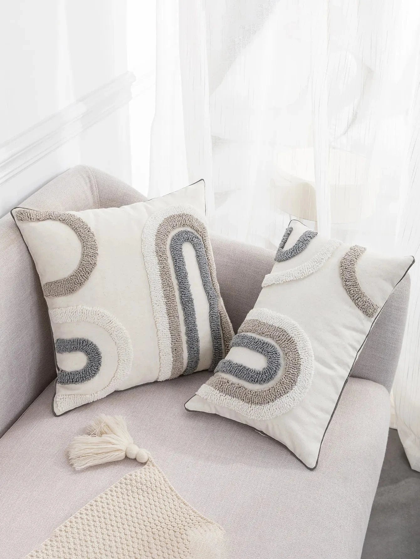 Coussins décoratifs en tissu beige et gris avec motifs abstraits, posés sur un canapé moderne et élégant
