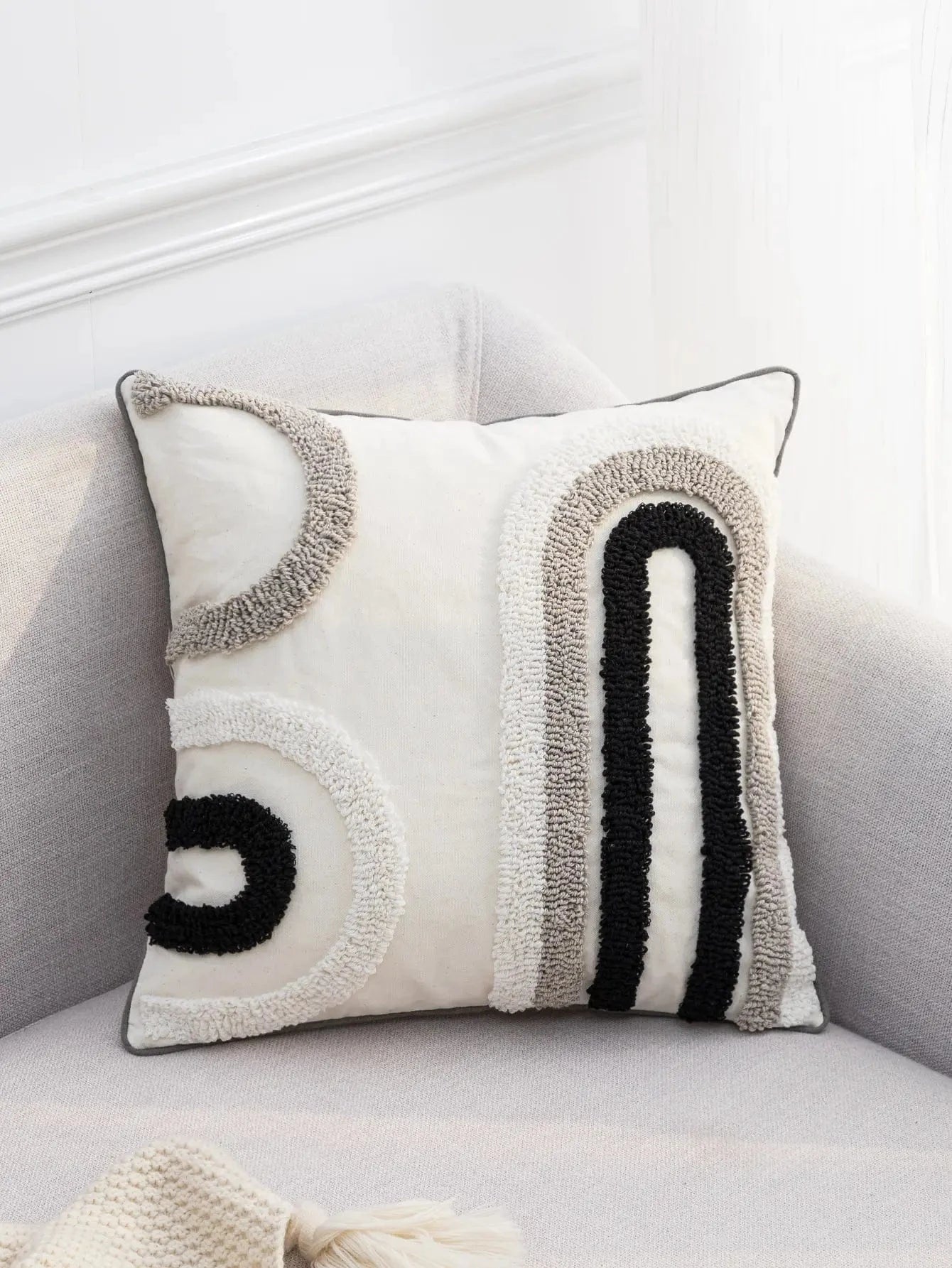 Coussin décoratif en tissu beige avec motifs abstraits noirs et gris, posé sur un canapé moderne