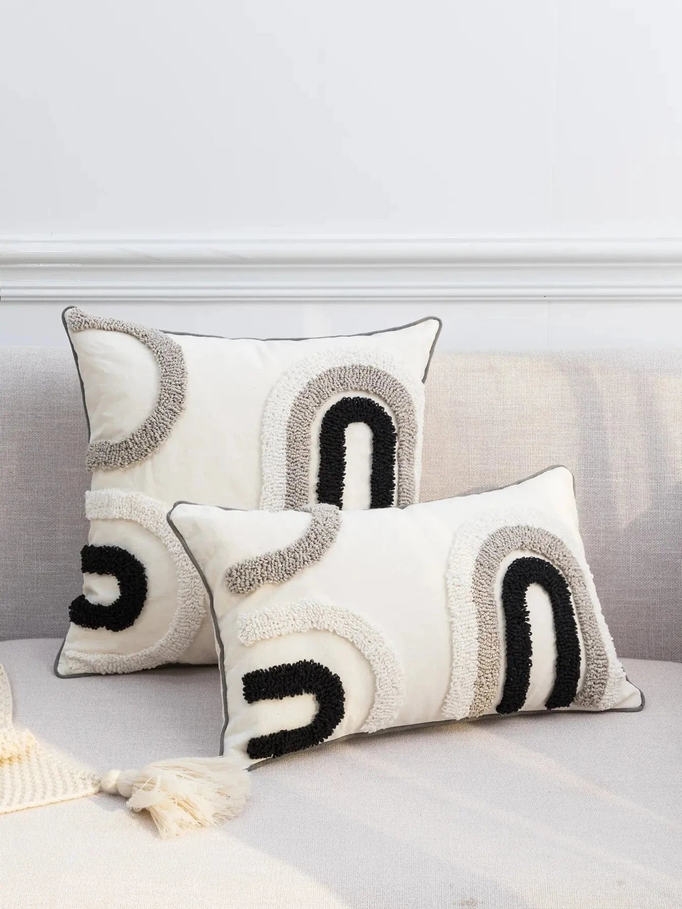 Coussins décoratifs en tissu beige avec motifs en noir et gris, posés sur un canapé moderne