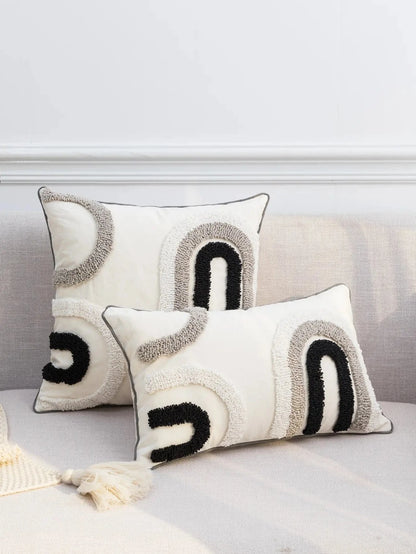 Coussins décoratifs en tissu beige avec motifs en noir et gris, posés sur un canapé moderne