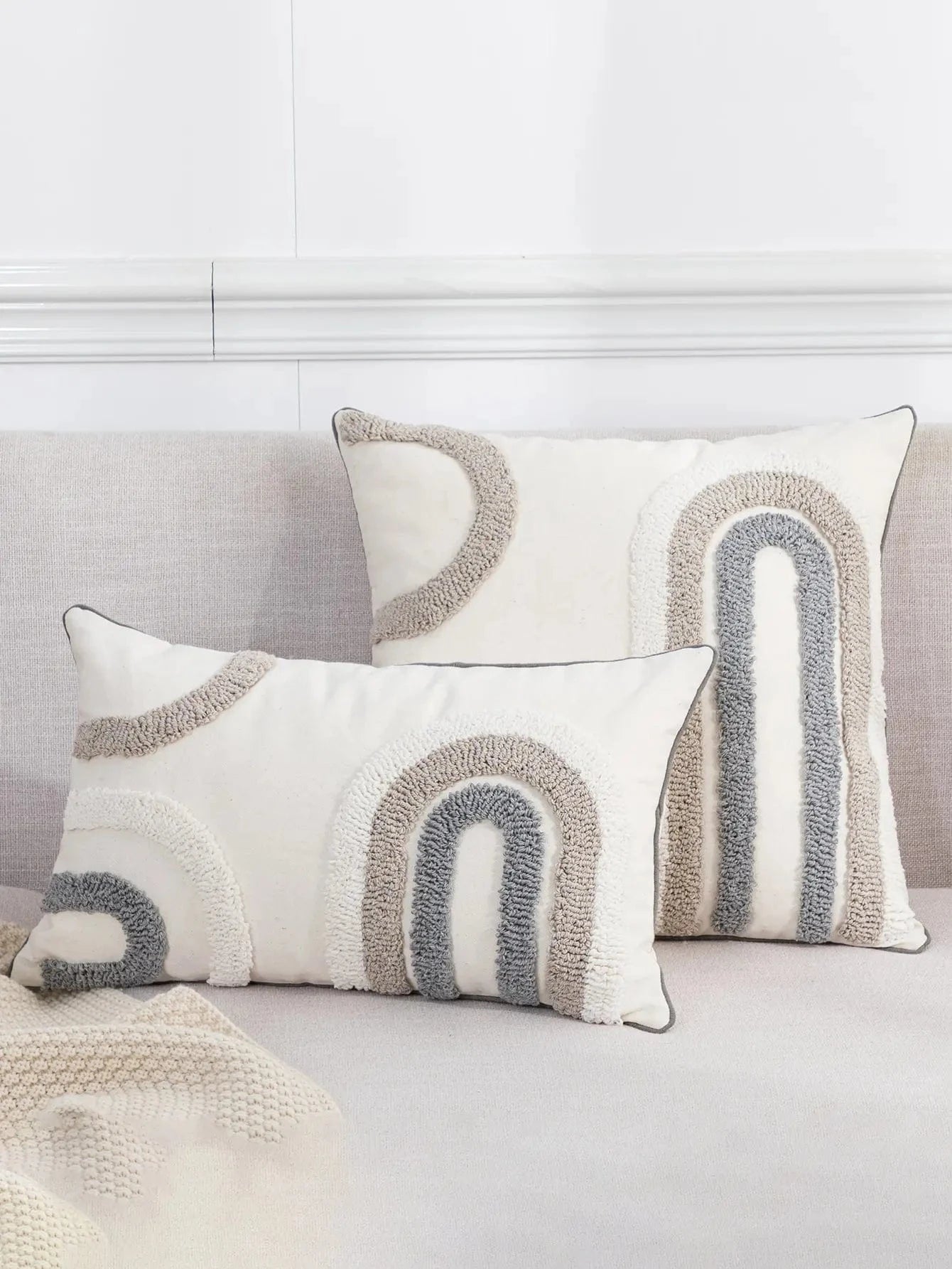 Coussins décoratifs aux motifs en arc, couleurs beige et gris, sur un canapé moderne et élégant