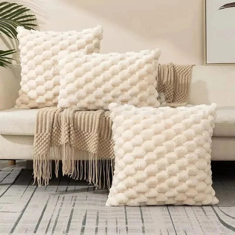 Coussins décoratifs en matière douce et texturée, couleur crème, disposés sur un canapé moderne avec un plaid