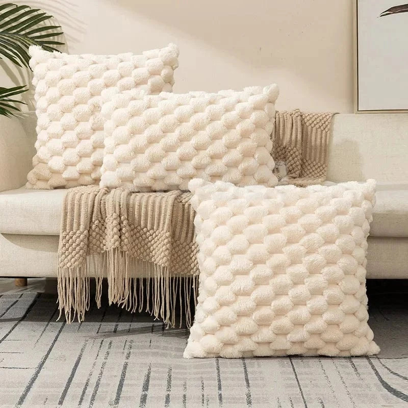 Coussins décoratifs en tissu doux et texturé, couleur crème, disposés sur un canapé avec un plaid beige