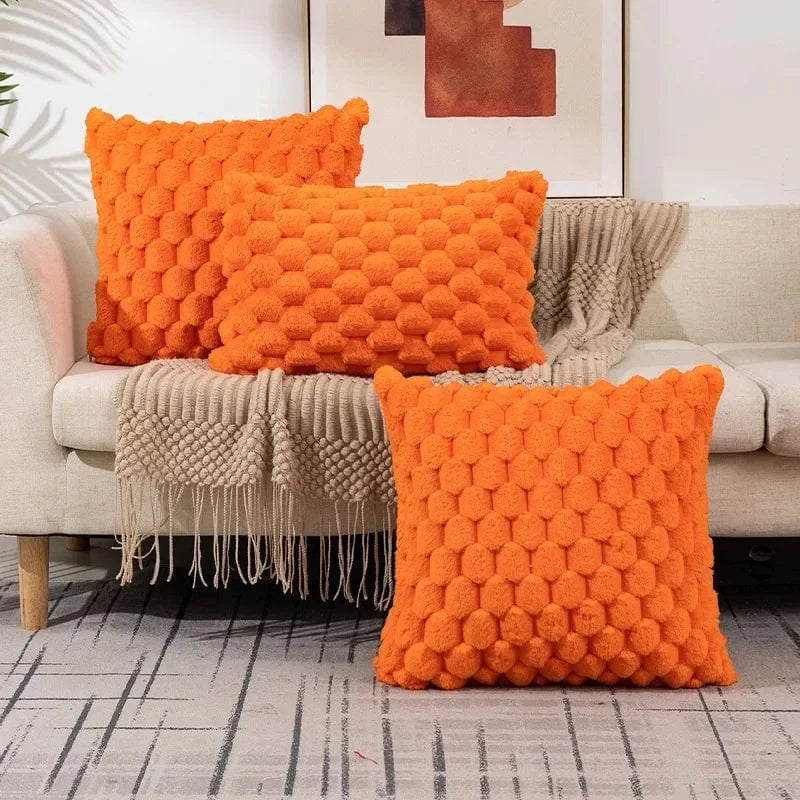 Coussins décoratifs orange en matière douce avec motifs en relief, disposés sur un canapé moderne et élégant