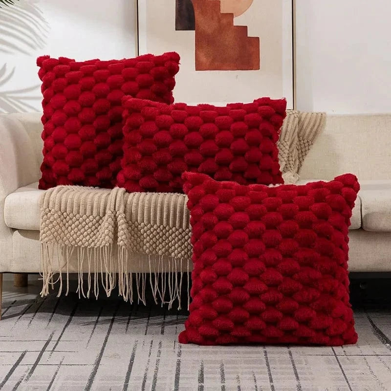 Trois coussins décoratifs rouges en velours texturé sur un canapé beige, ajoutant une touche chaleureuse à l'intérieur
