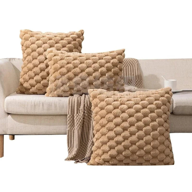 Coussins décoratifs en velours beige à motifs texturés, disposés sur un canapé clair avec un plaid