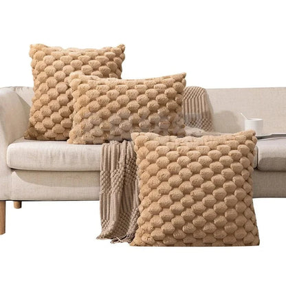 Coussins décoratifs en velours beige à motifs texturés, disposés sur un canapé clair avec un plaid