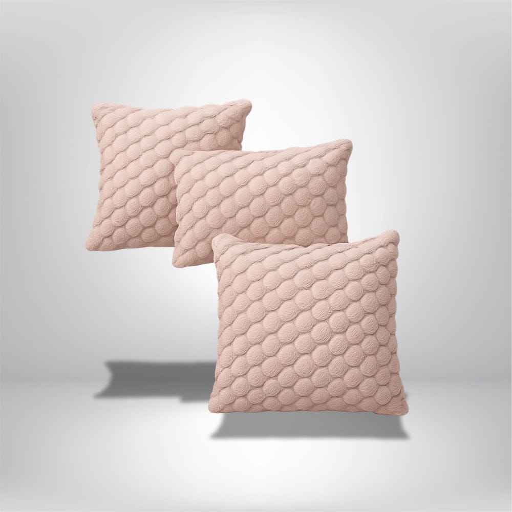 Trois coussins décoratifs en tissu rose avec un motif en relief, posés sur un fond neutre