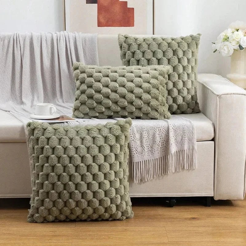 Coussins décoratifs en velours vert, motifs en relief, disposés sur un canapé avec un plaid beige