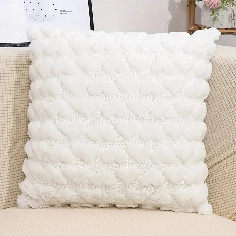 Coussin décoratif blanc en forme de cœur, placé sur un canapé beige, apportant une touche douce et romantique