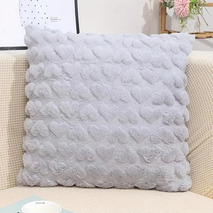 Coussin décoratif en velours gris avec motif en forme de cœurs, posé sur un canapé beige