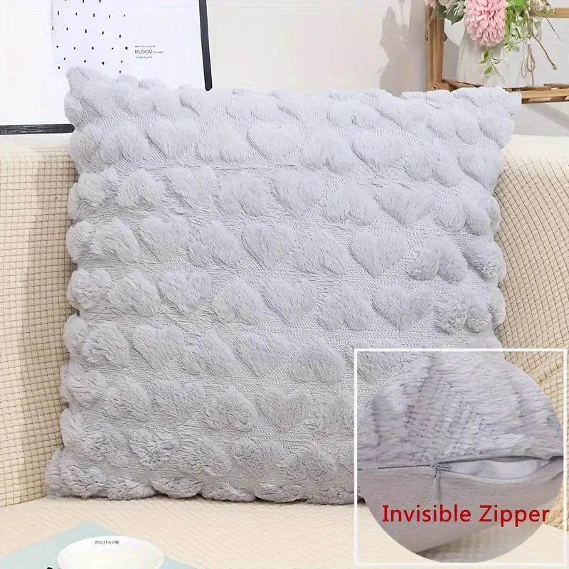 Coussin décoratif en velours gris avec motifs en forme de cœur, posé sur un canapé beige, ajoutant une touche douce