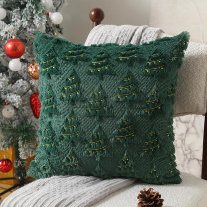 Coussin décoratif vert en velours avec motifs de sapins dorés, posé sur un fauteuil à côté d'un sapin de Noël