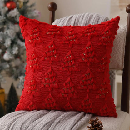 Coussin décoratif rouge avec motifs de sapins dorés, posé sur un fauteuil en tissu dans un salon chaleureux